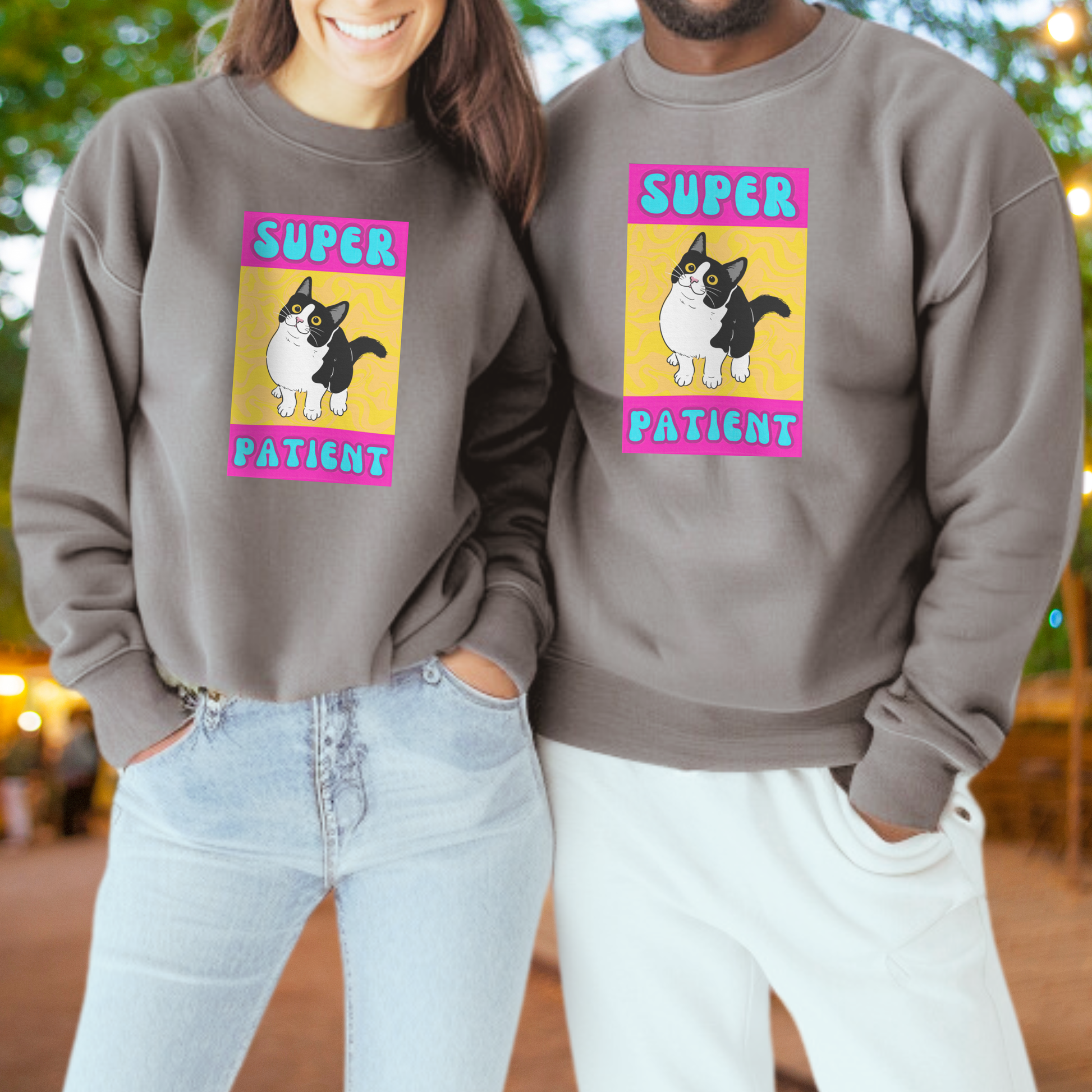 A woman and a man are standing next to each other, both wearing gray sweatshirts with a cartoon cat and the text "SUPER PATIENT" printed on them.