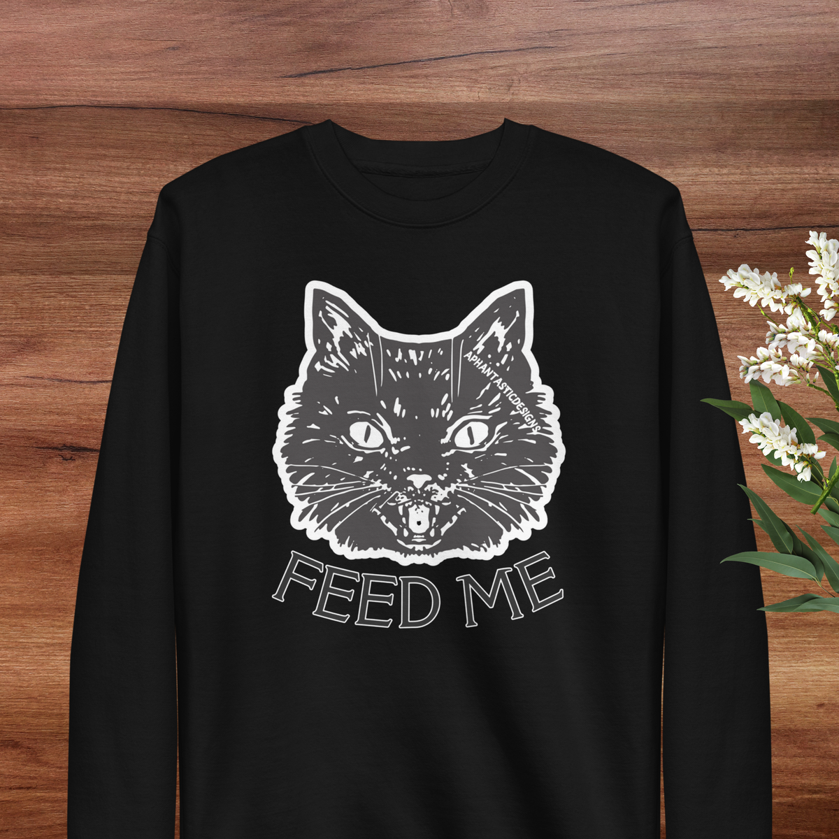 A black long-sleeved shirt with a white graphic of a cat's face and the text "FEED ME" printed on it.