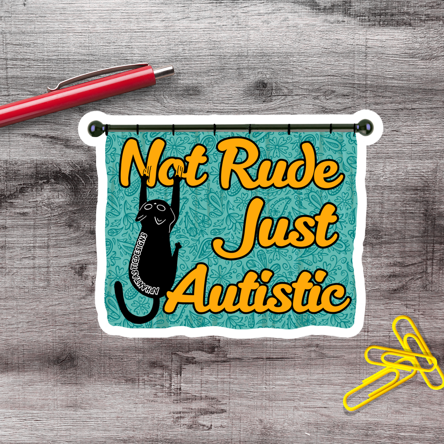 A sticker with the text "Not Rude Just Autistic" and a black cat graphic, placed on a wooden surface next to a red pen and yellow paper clips.