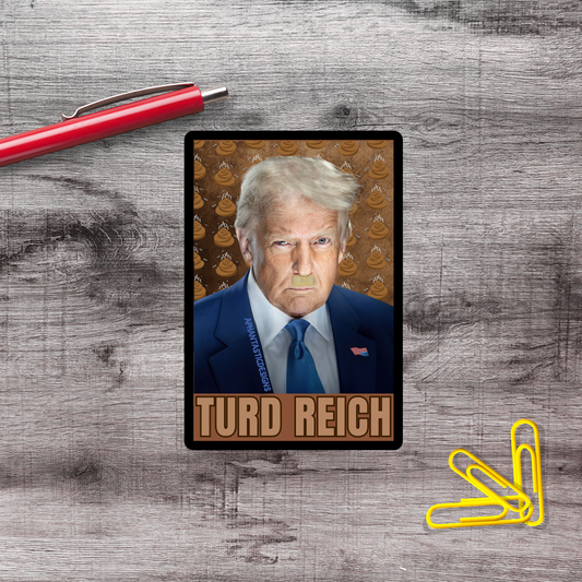 A political campaign card featuring a man with blonde hair and a blue suit, with the name 'TURD REICH' printed on it. The card is placed on a wooden surface, with a red pen and yellow paper clips nearby.