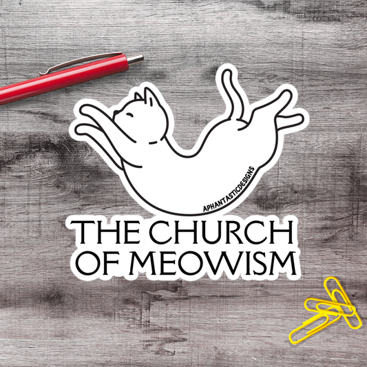A sticker depicting a cat in a playful pose, with the text "THE CHURCH OF MEOWWISM" below it, is placed on a wooden surface alongside a red pen and yellow paper clips.