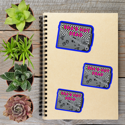 a spiral notebook with three stickers on it, along with several potted plants arranged on a wooden surface.