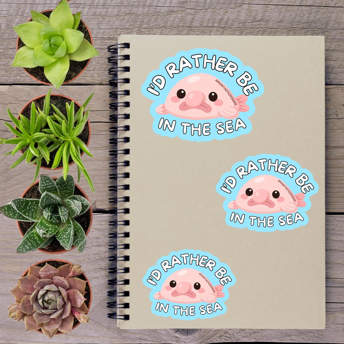 a notebook with stickers on it, along with several potted plants arranged on a wooden surface.
