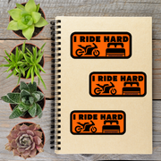 a spiral notebook with three stickers on it, along with four potted plants arranged on a wooden surface.