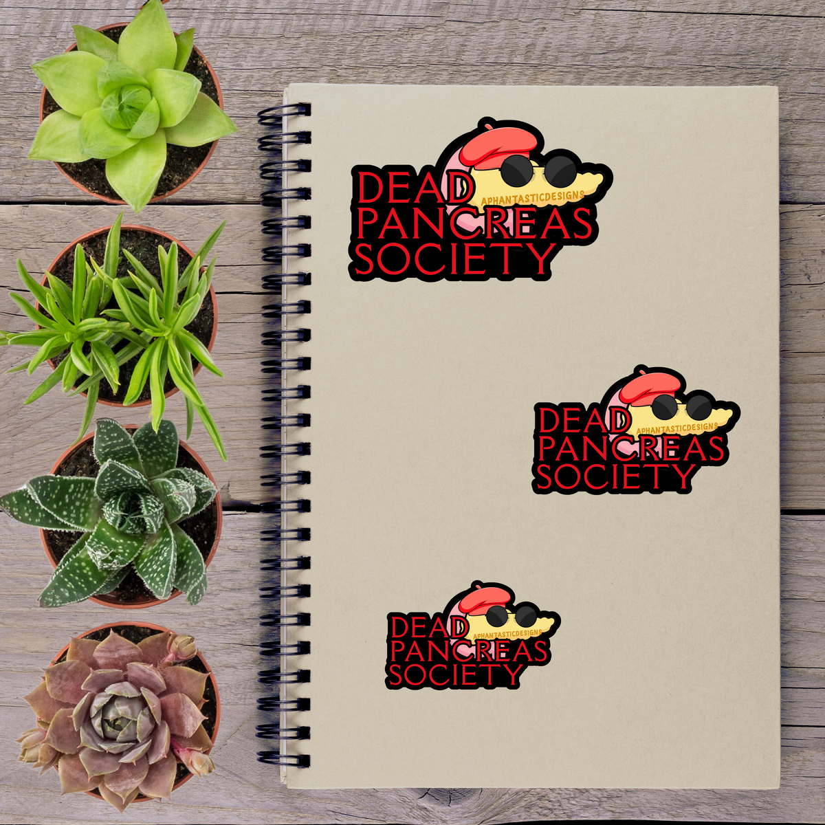 a spiral notebook with stickers on it, surrounded by four potted plants.
