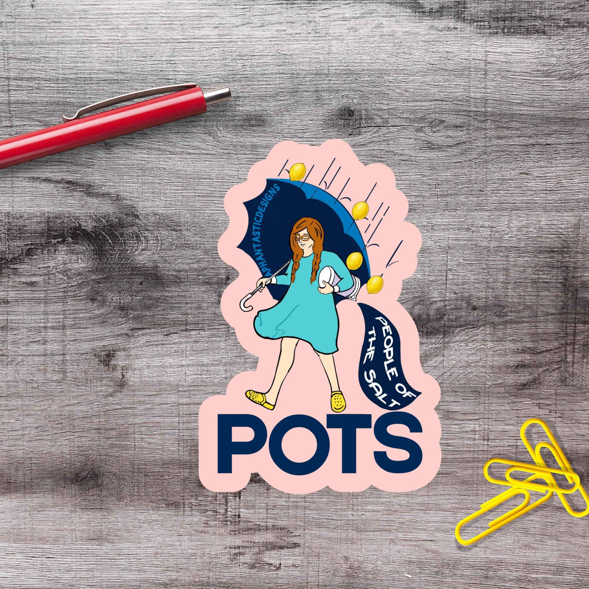 A sticker with a cartoon illustration of a woman holding an umbrella and the text "POTS" is placed on a wooden surface next to a red pen and yellow paper clips.