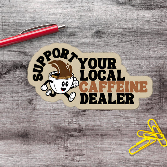 A sticker with a cartoon coffee cup and the text "Support Your Local Caffeine Dealer" on a wooden surface.