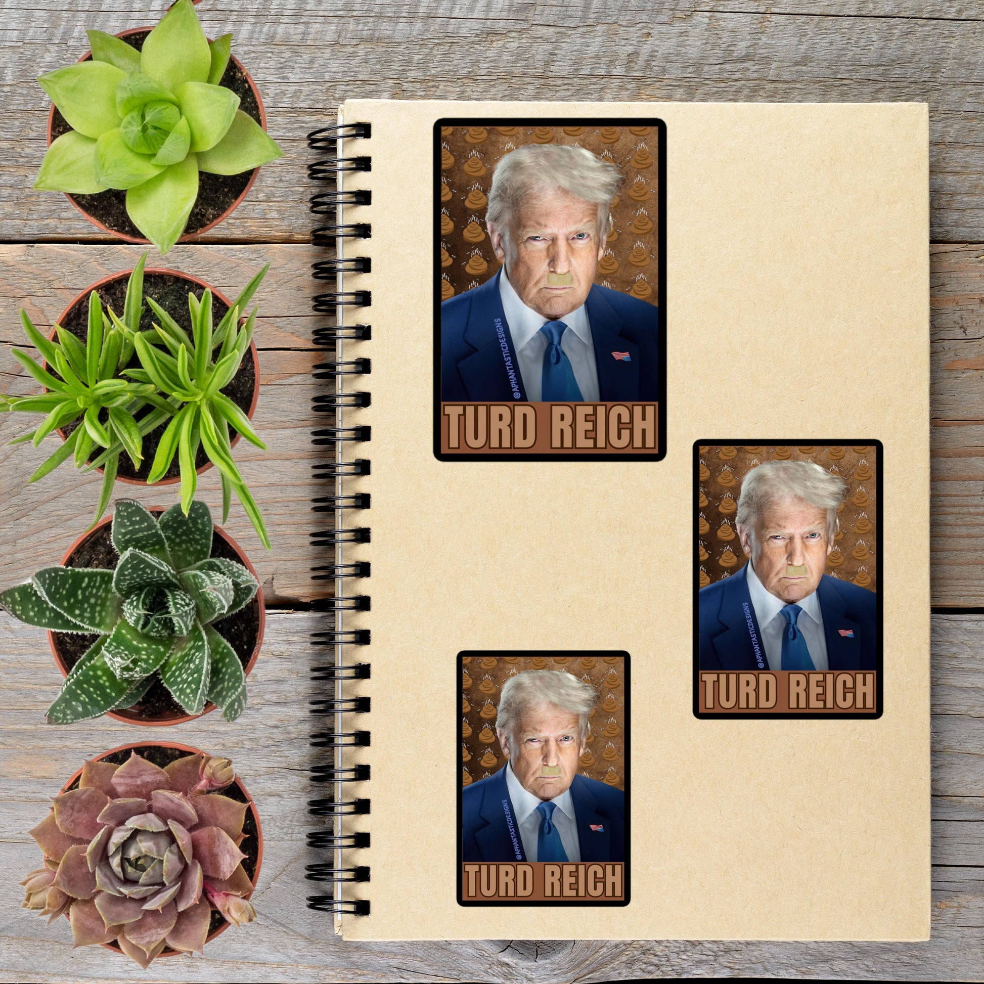 a spiral notebook with three identical stickers of Donald Trump, each depicting a different angle of the president. The stickers are arranged on a wooden surface alongside several potted plants.