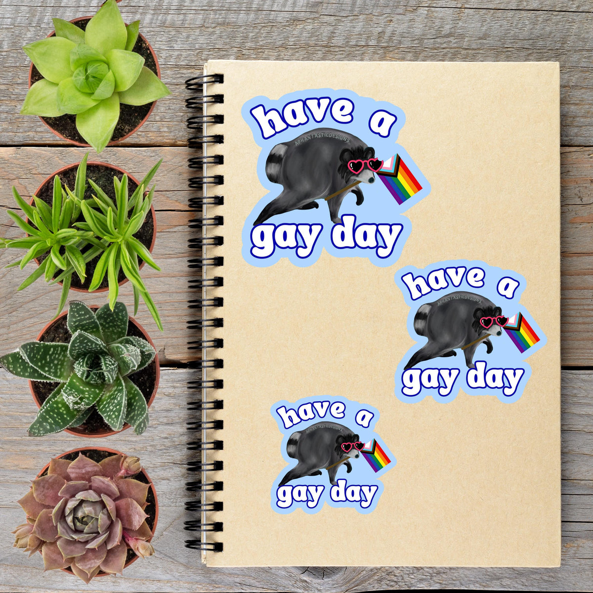 a spiral notebook with stickers on it, along with several potted plants arranged on a wooden surface.