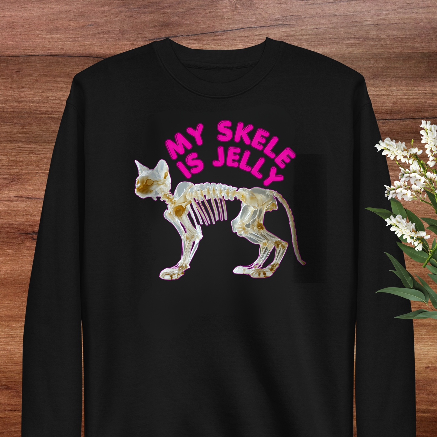 A black long-sleeved shirt with a graphic design depicting a skeleton of a cat in pink and white colors, along with the text "MY SKLE IS JELLY" in pink letters.
