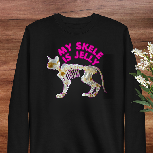 A black long-sleeved shirt with a graphic design depicting a skeleton of a cat in pink and white colors, along with the text "MY SKLE IS JELLY" in pink letters.