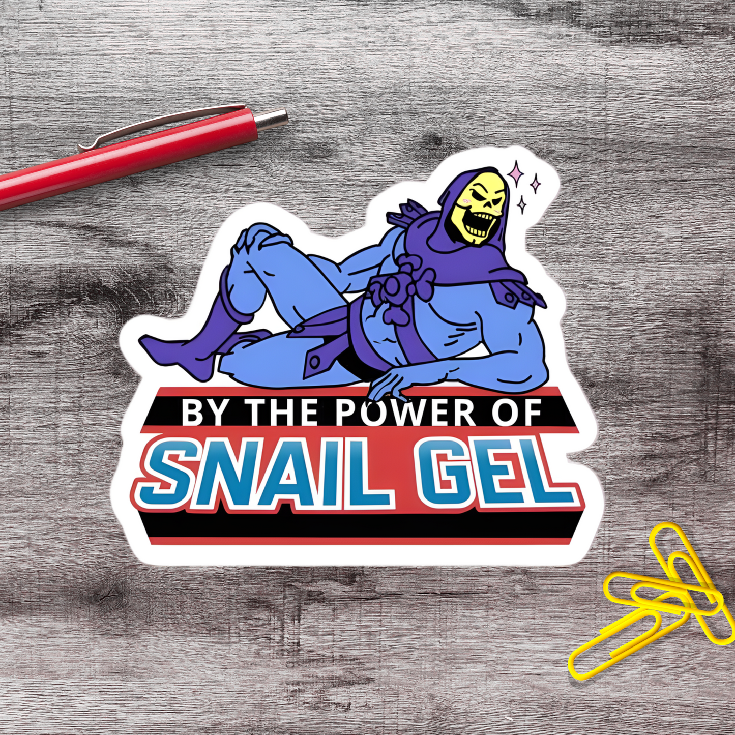 A sticker featuring a cartoon character with a skeleton mask and the text "By the power of snail gel" on a wooden surface.