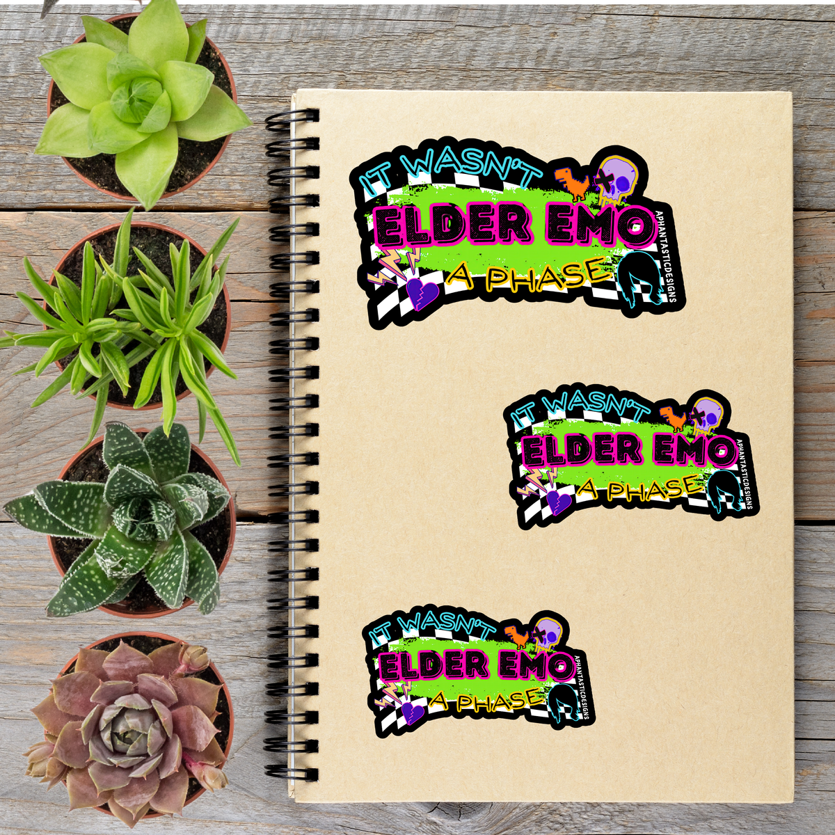 a spiral notebook with three stickers on it, along with four potted plants arranged on a wooden surface.