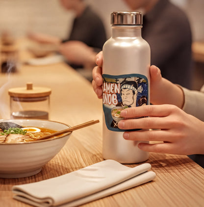 A person is holding a water bottle with a label featuring a cartoon character, while sitting at a table with a bowl of food and a glass.