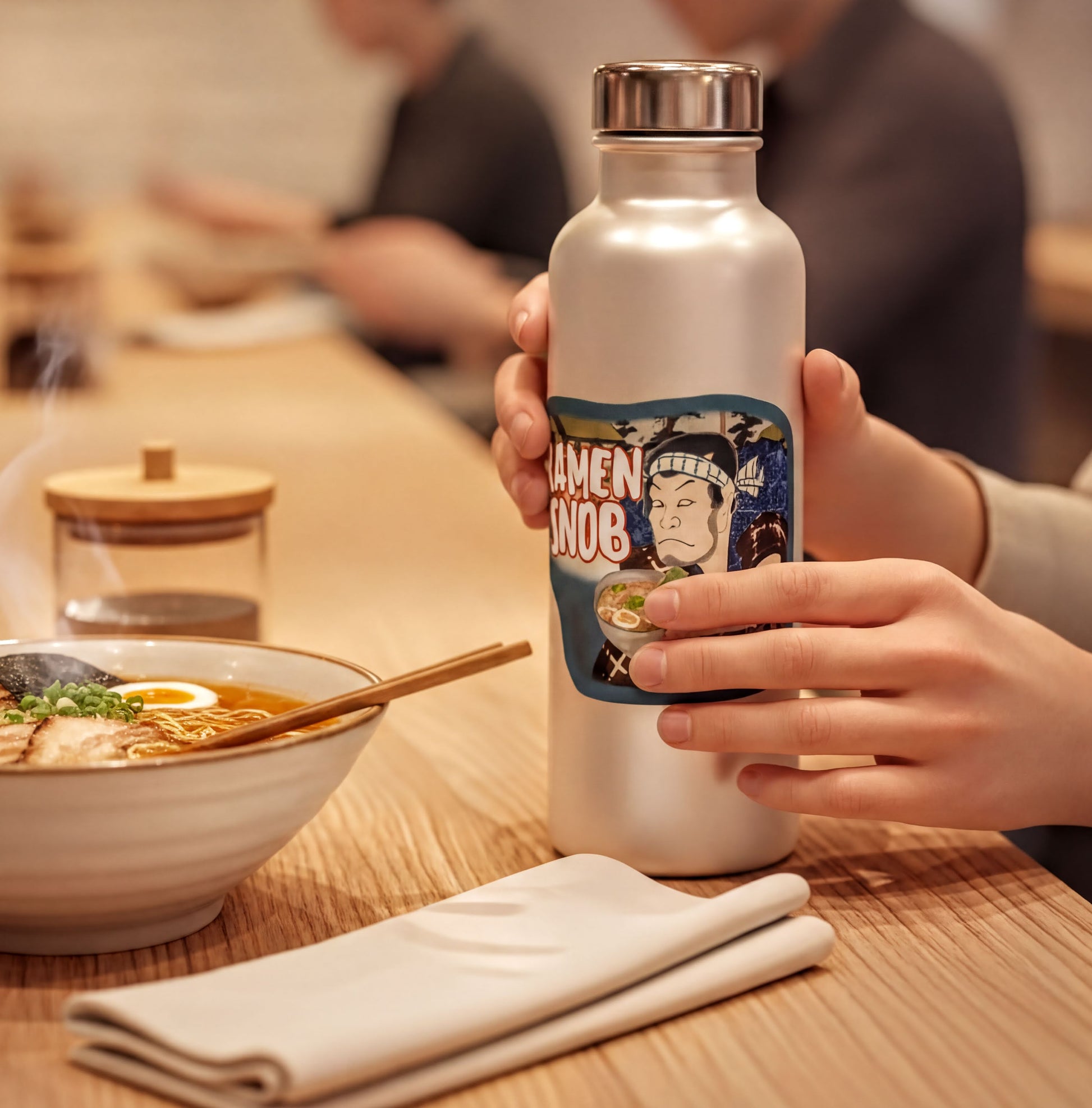 A person is holding a water bottle with a label featuring a cartoon character, while sitting at a table with a bowl of food and a glass.
