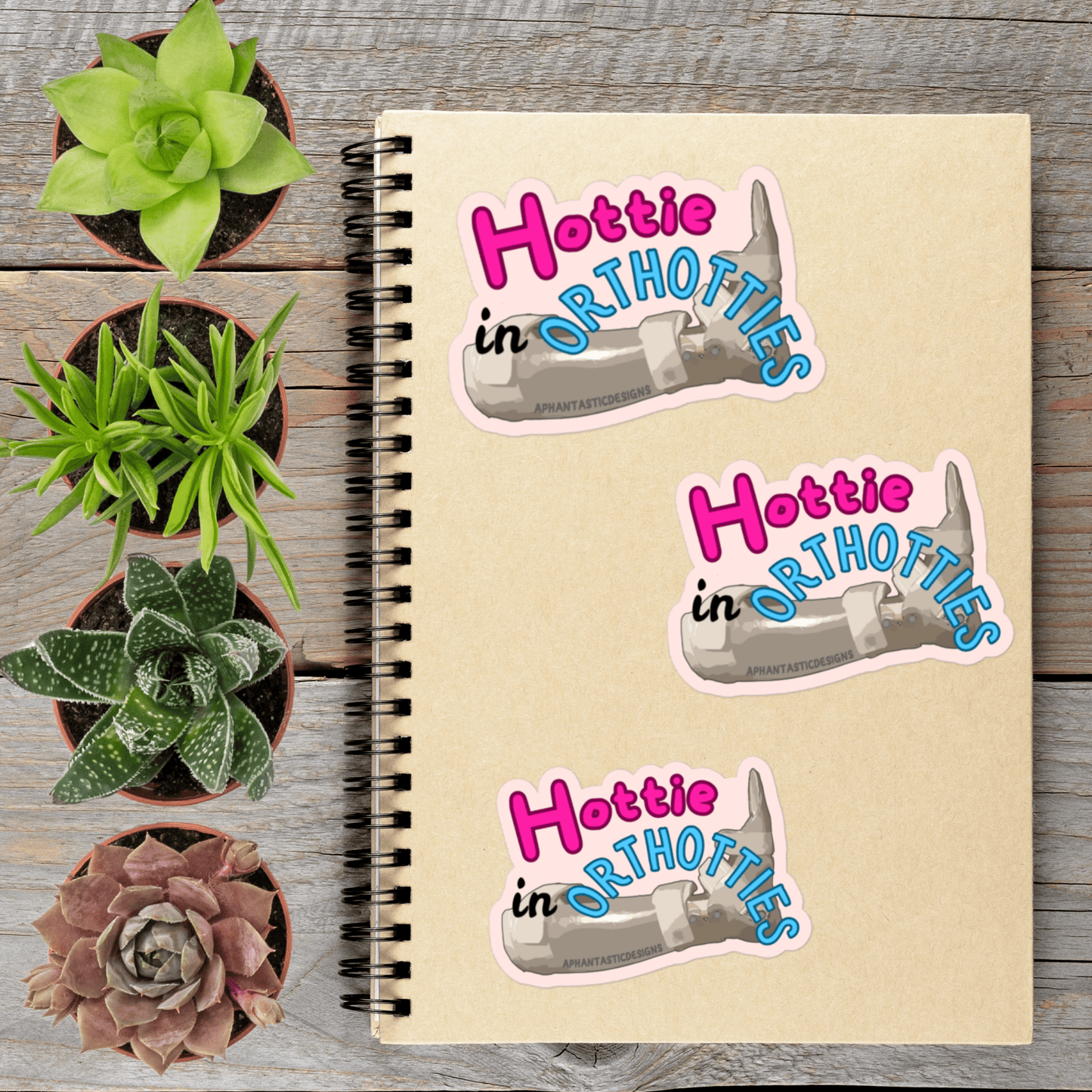 a notebook with stickers on it, surrounded by potted plants on a wooden surface.