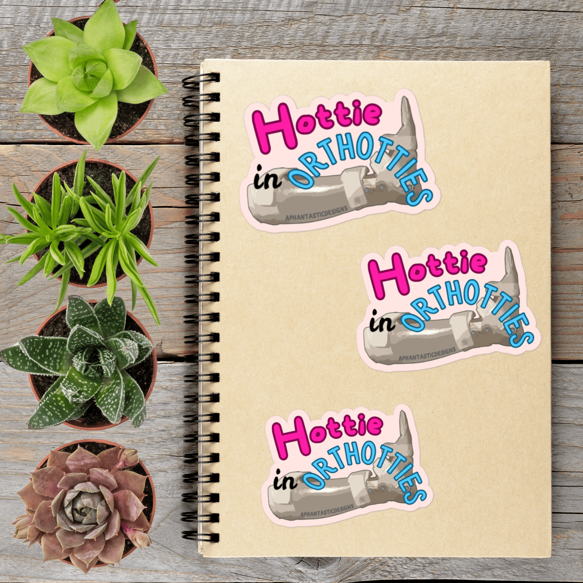 a notebook with stickers on it, surrounded by potted plants on a wooden surface.