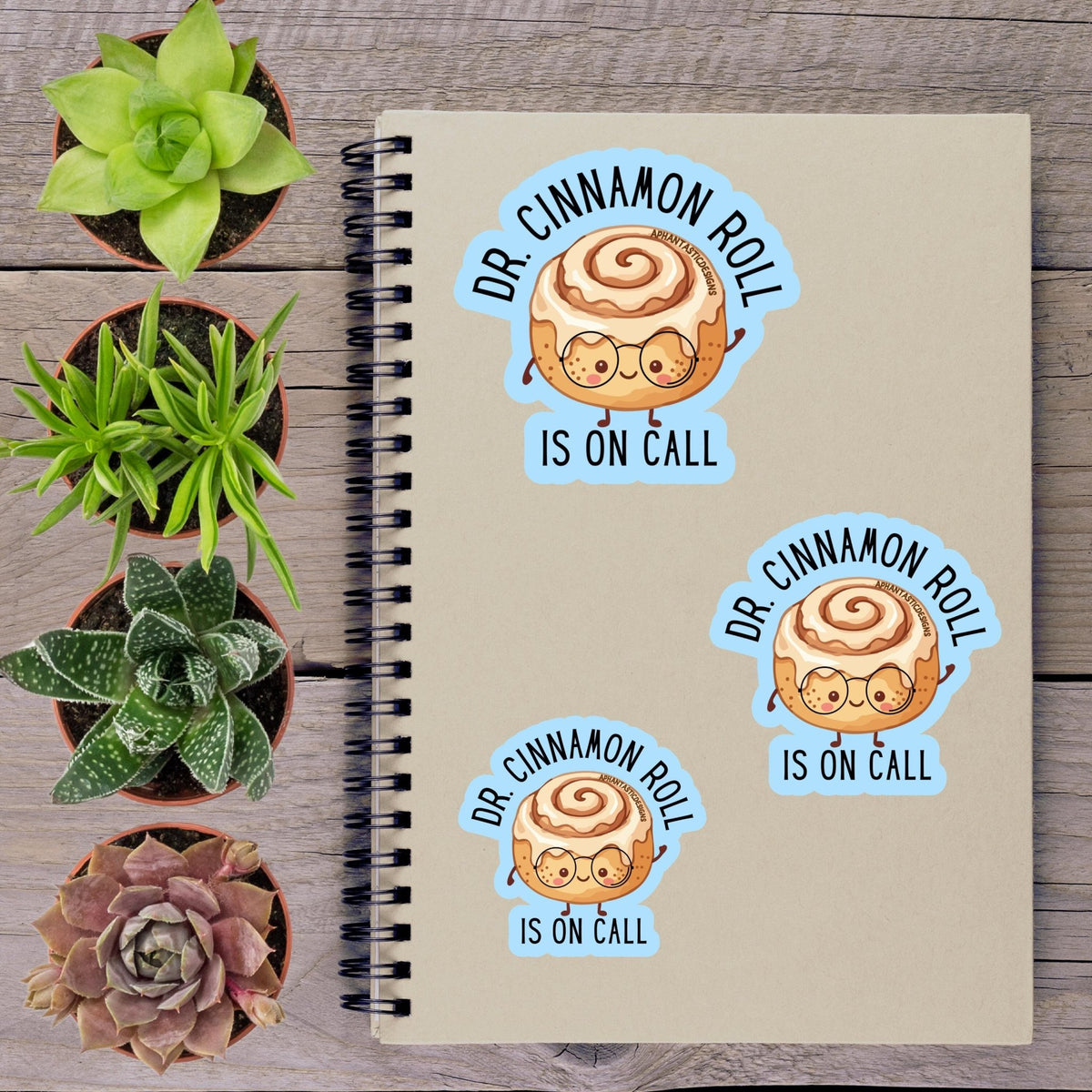 a notebook with stickers on it, along with several potted plants arranged on a wooden surface.