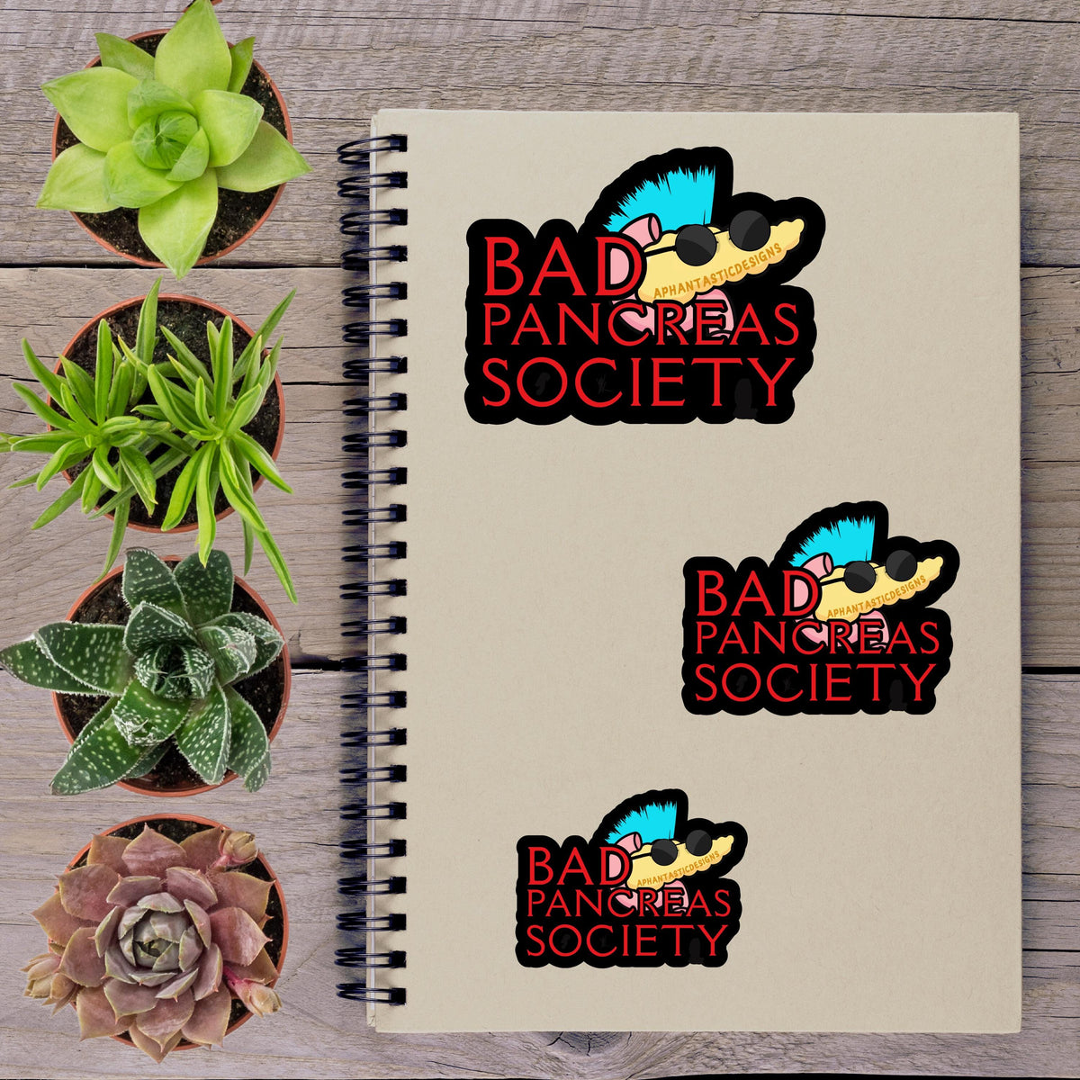 a spiral notebook with stickers on it, along with several potted plants arranged on a wooden surface.