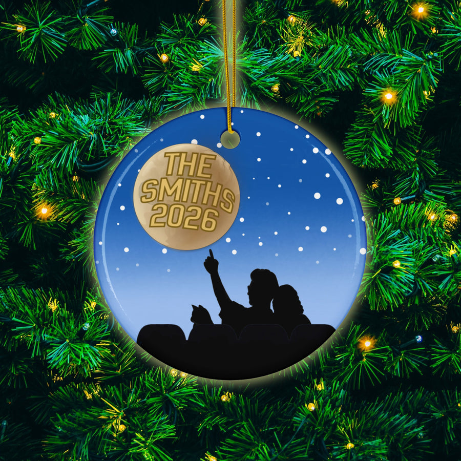 A Christmas ornament with a silhouette of a person pointing upwards, surrounded by a starry night sky and a tree with green needles.