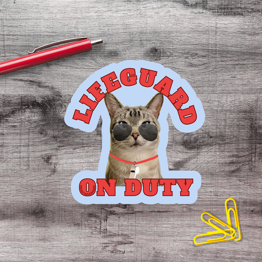 A sticker with a cat wearing sunglasses and the text "LIFEGUARD ON DUTY" on a wooden surface.