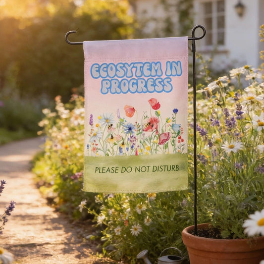 A garden path lined with colorful flowers and plants, with a sign hanging from a metal pole that reads "ECOSYSTM IN PROGRESS" and "PLEASE DO NOT DISTURB".