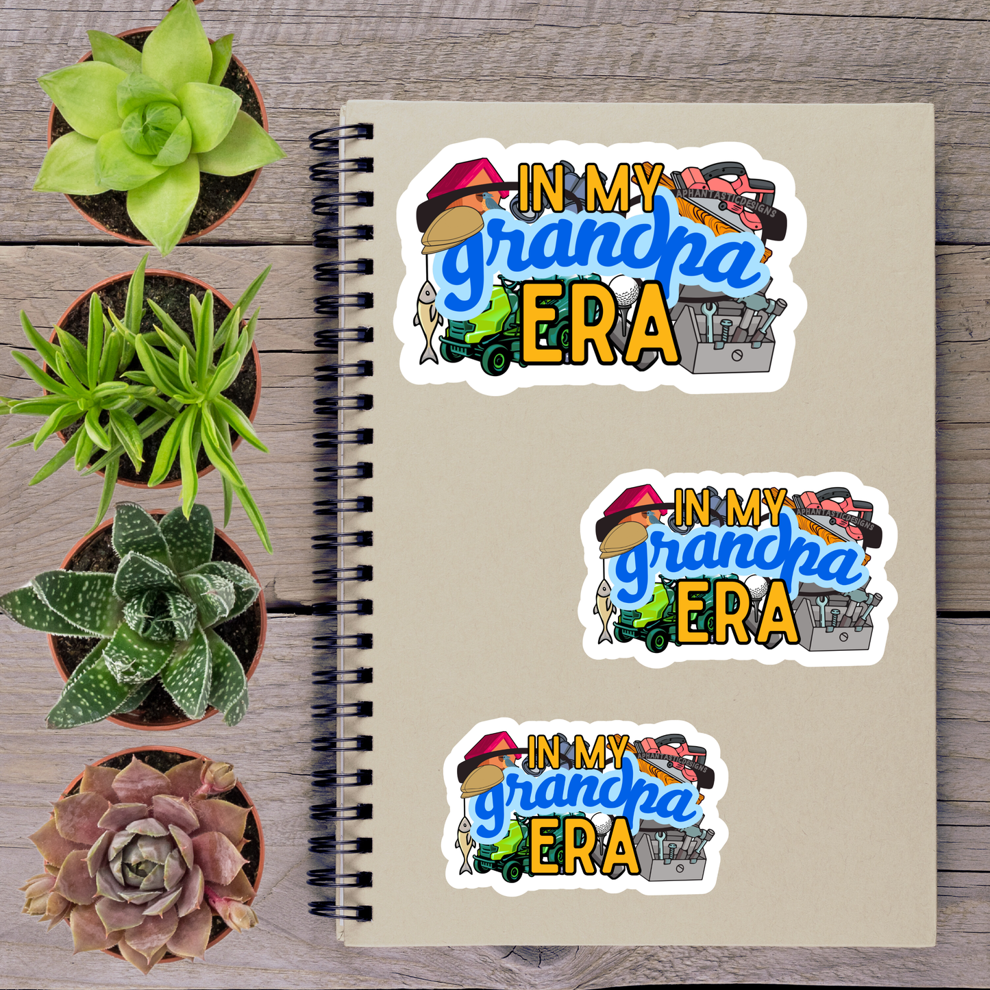 a spiral notebook with three stickers on it, along with several potted plants arranged on a wooden surface.