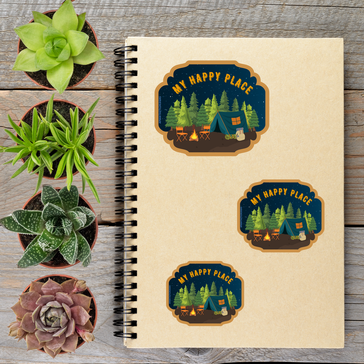 a spiral-bound notebook with stickers on it, along with several potted plants arranged on a wooden surface.