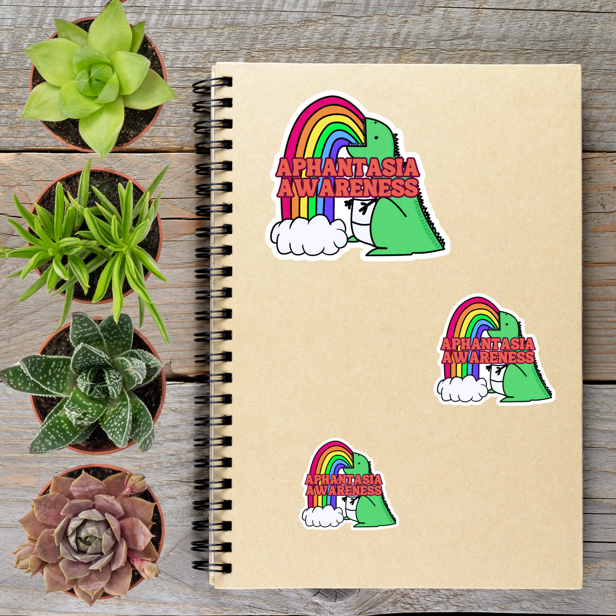a spiral notebook with stickers on it, surrounded by potted plants on a wooden surface.
