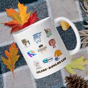 A white mug with various colorful stickers and illustrations on it, placed on a table with autumn leaves and pine cones.