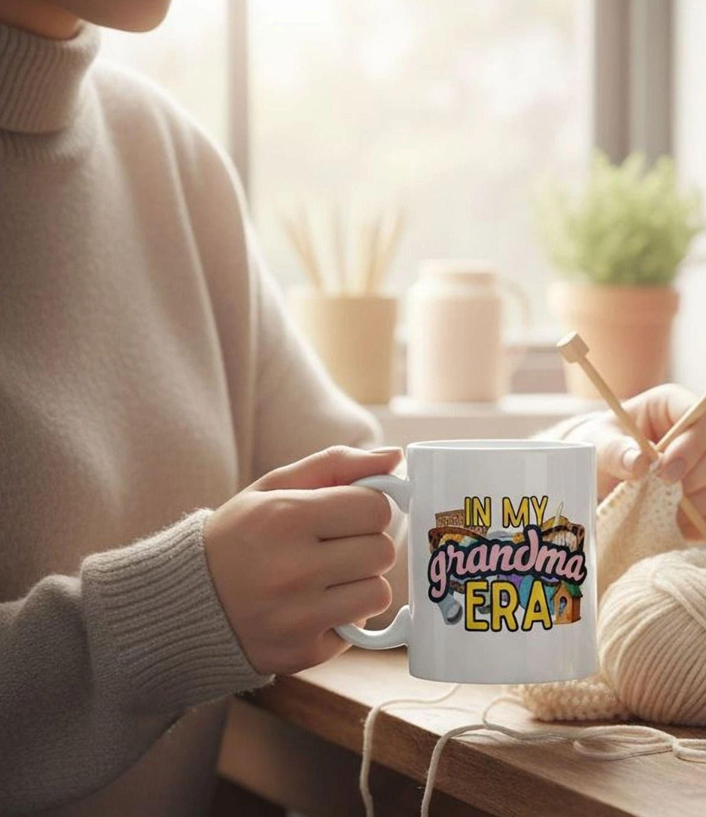 A person is sitting at a table, holding a mug with the text "IN MY GRANDMA ERA" printed on it.