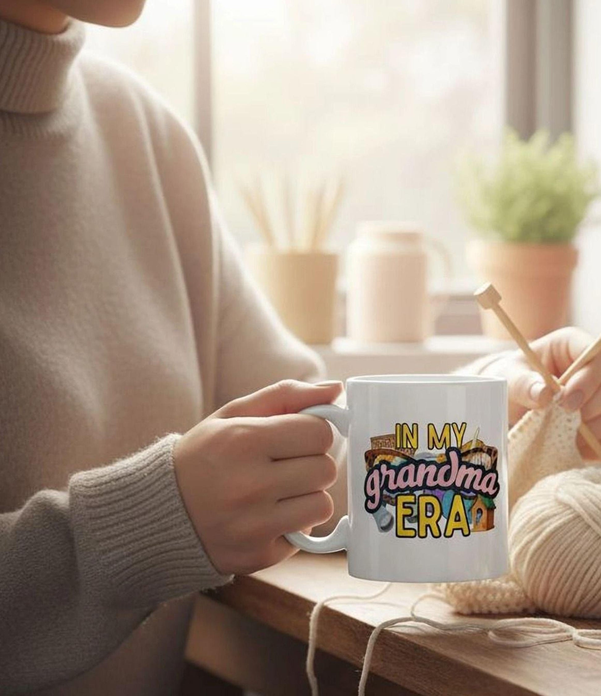 A person is sitting at a table, holding a mug with the text "IN MY GRANDMA ERA" printed on it.