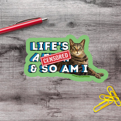 A sticker with a cat and the text "LIFE'S A CENSORED & SO AM I" on a wooden surface.