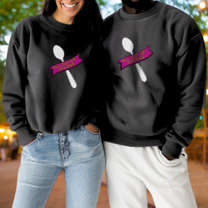 A woman and a man are standing next to each other, both wearing black sweatshirts with a graphic design featuring a spoon and a pink banner with the text "ALL OUTSOURCES".