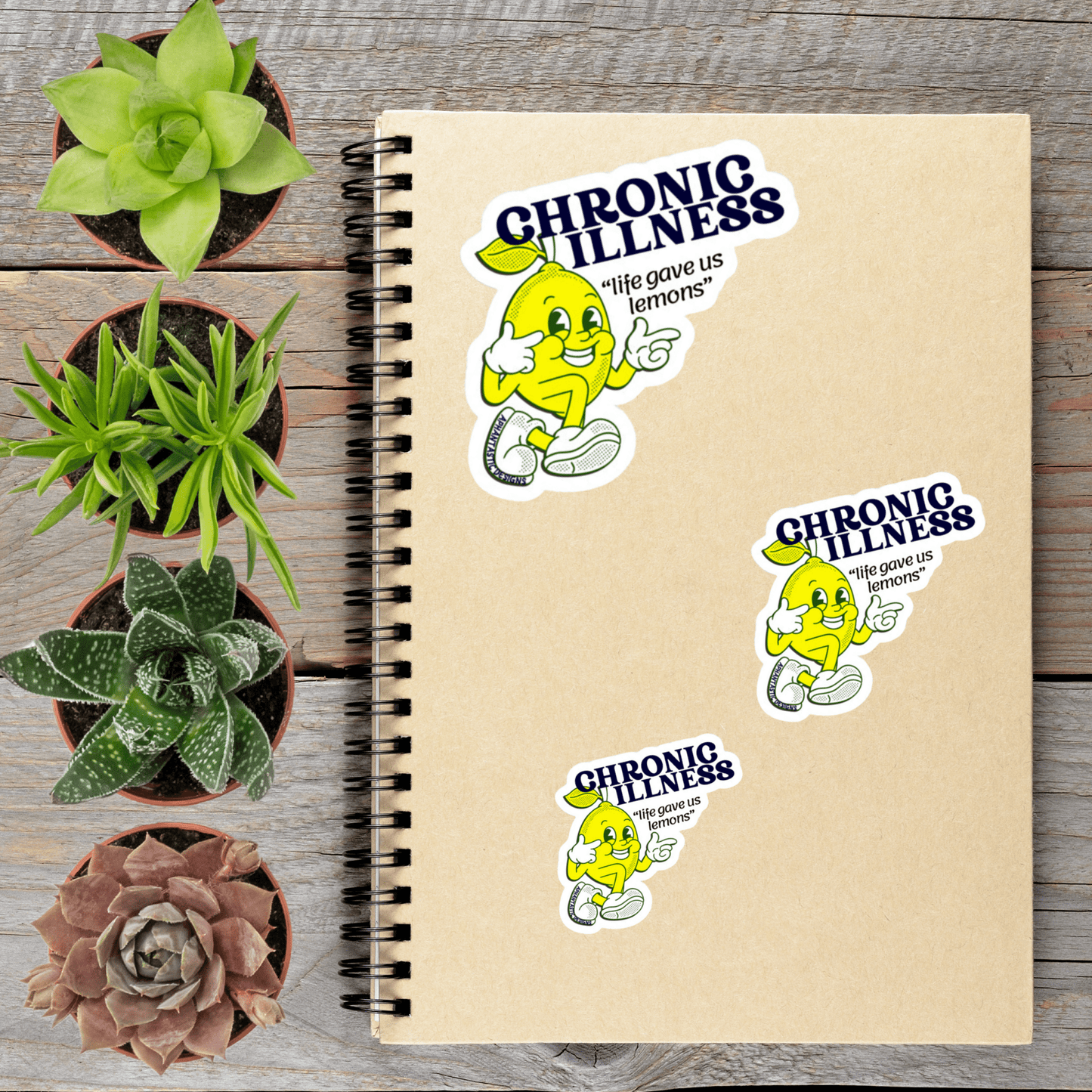 a notebook with stickers on it, along with several potted plants arranged on a wooden surface.