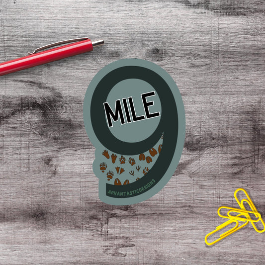 a sticker with the word "MILES" on it, along with some paw prints, placed on a wooden surface. There is also a red pen and a pile of yellow paper clips nearby.