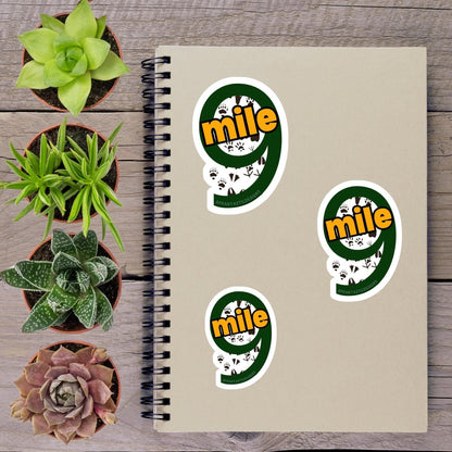 a spiral notebook with stickers on it, surrounded by four potted plants of different sizes and shapes, all placed on a wooden surface.