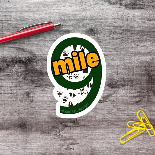 a sticker with the number 9 and the word "mile" on a wooden surface, along with a red pen and yellow paper clips.