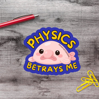 a sticker with a pink fish and the text "Physics Betrays Me" on a wooden surface.