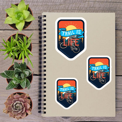 a spiral-bound notebook with three stickers on it, along with several potted plants arranged on a wooden surface.