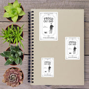 a spiral notebook with three stickers on it, placed on a wooden surface alongside several potted plants.