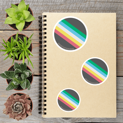 a spiral-bound notebook with three colorful stickers on it, placed on a wooden surface alongside several potted succulent plants.