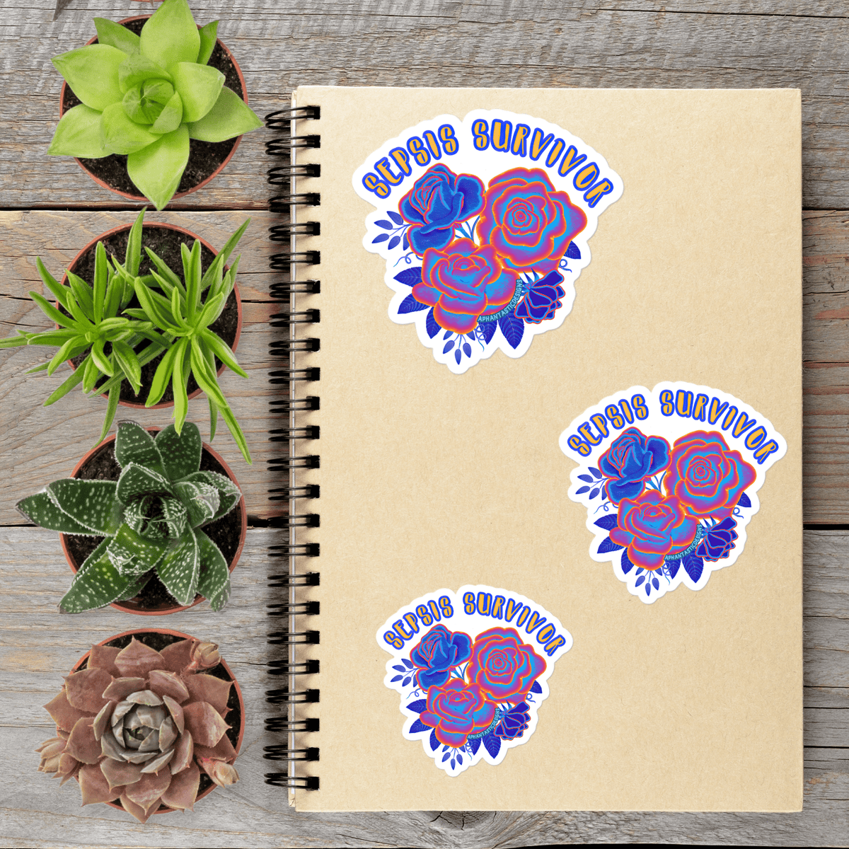 a spiral-bound notebook with three stickers on it, surrounded by four potted succulent plants on a wooden surface.