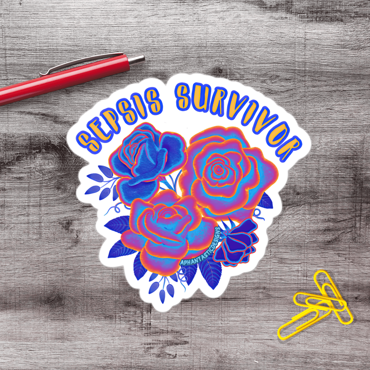 A sticker with a floral design and the text "SILIPS SURVIVOR" is placed on a wooden surface next to a red pen and yellow paper clips.