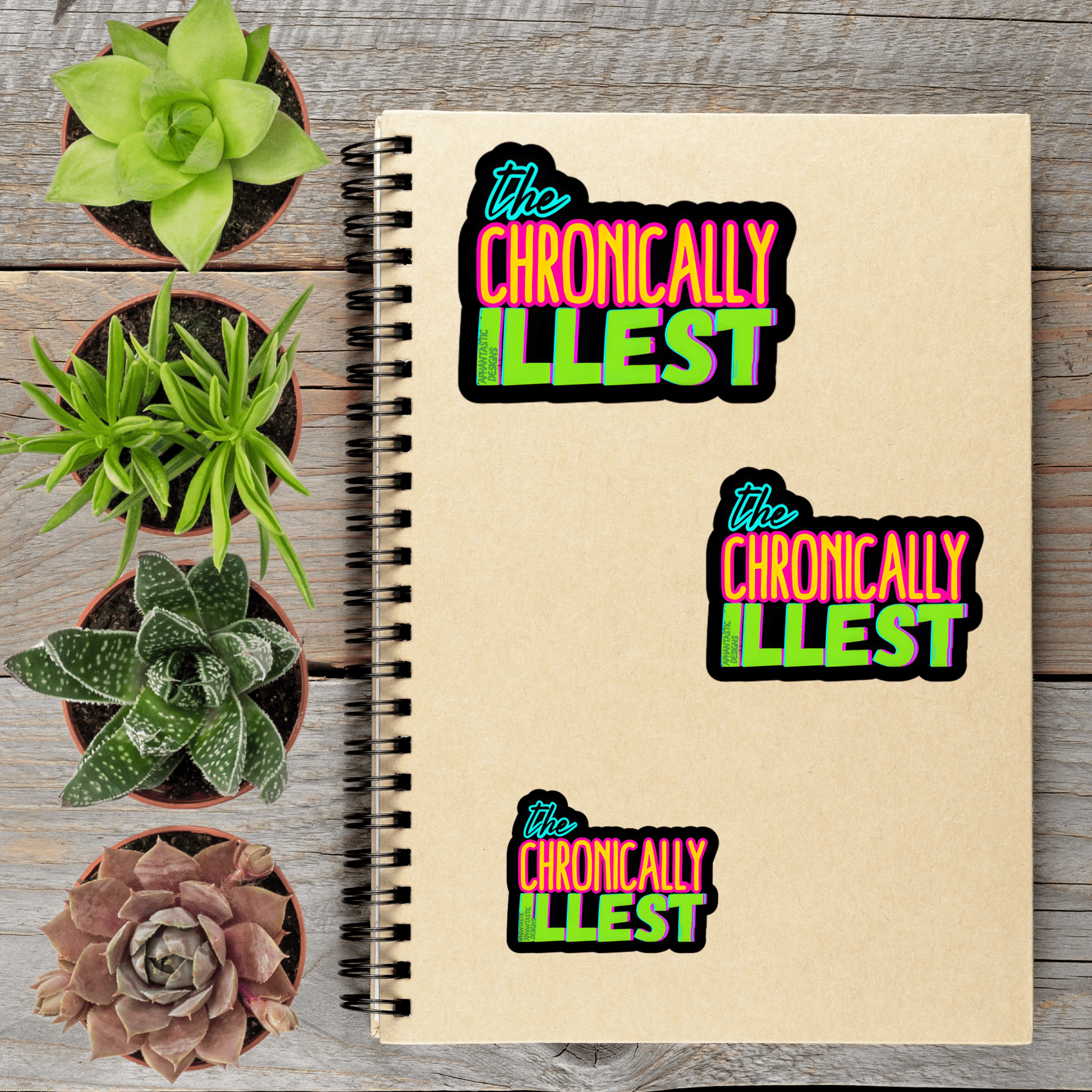 a spiral notebook with three stickers on it, along with four potted succulent plants arranged on a wooden surface.