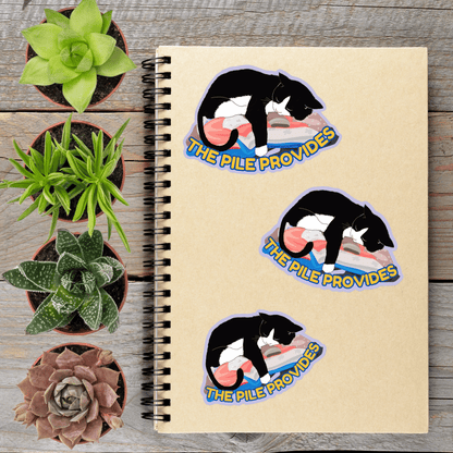 a spiral notebook with three stickers on it, each depicting a black and white cat sleeping on a pile. The stickers are arranged in a row on the notebook, with the first sticker on the left, the second sticker in the middle, and the third sticker on the right. The stickers are placed next to several potted plants, creating a visually appealing and organized display.