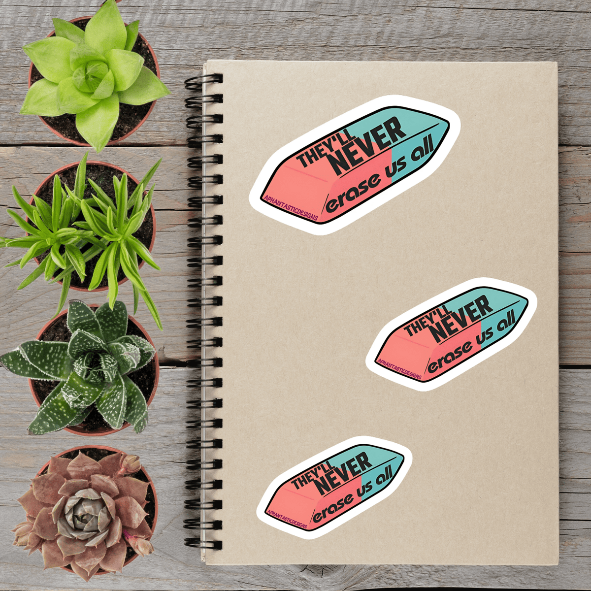 a spiral notebook with three stickers on it, along with four potted succulent plants arranged on a wooden surface.