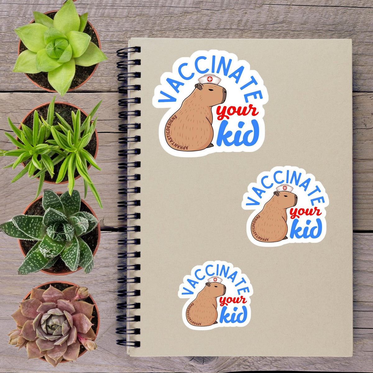 a notebook with stickers on it, along with several potted plants arranged on a wooden surface.